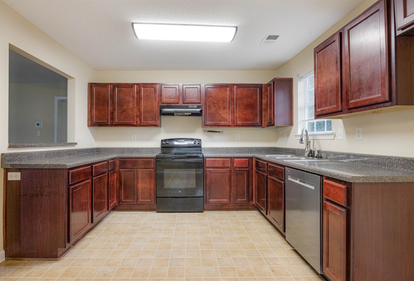 Kitchen featuring black electric range, reddish brown cabinets, dark countertops, dishwasher, and under cabinet range hood