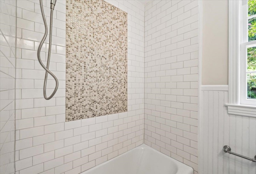 Bathroom featuring a subway tile shower surround with a mosaic accent wall, white tub, and a window with trim