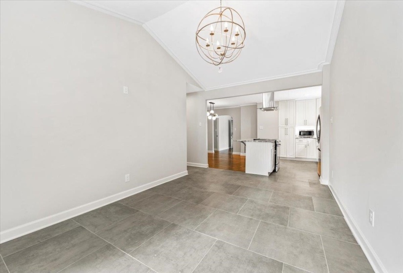 Spacious room featuring vaulted ceilings with crown molding, a large orb chandelier, and tile flooring