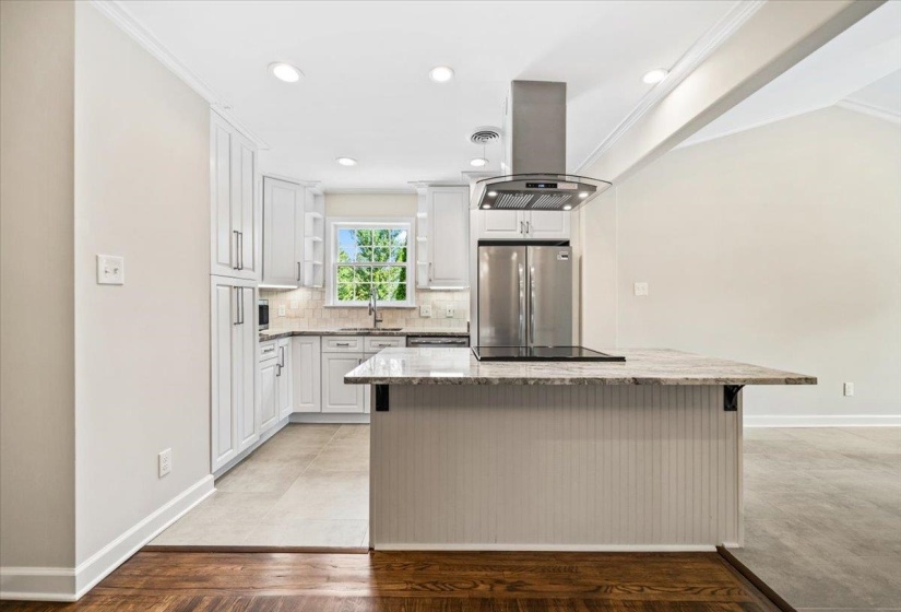 Contemporary kitchen featuring white cabinetry, a granite countertop island with a cooktop, a stainless steel range hood, and recessed lighting