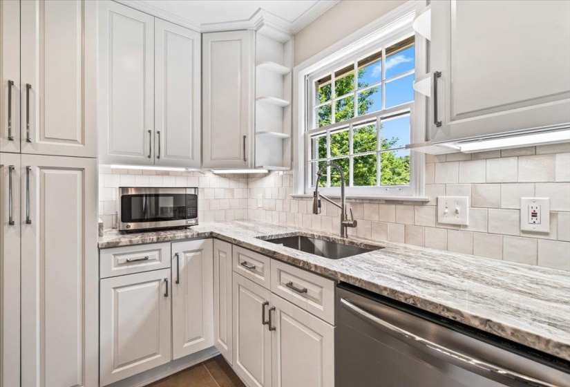 Kitchen featuring white shaker-style cabinetry, a stainless steel sink with a gooseneck faucet, light-toned countertops, subway tile backsplash, and under-cabinet lighting