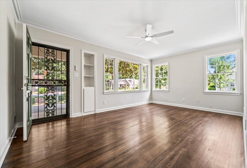 Spacious room featuring wood-finish flooring, a contemporary ceiling fan with integrated lighting, multiple pane windows, and a built-in shelving unit