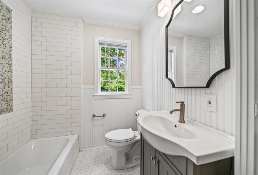 Bathroom featuring white subway tile surround, hexagonal floor tiling, a single vanity with an integrated sink, and an arched wall mirror
