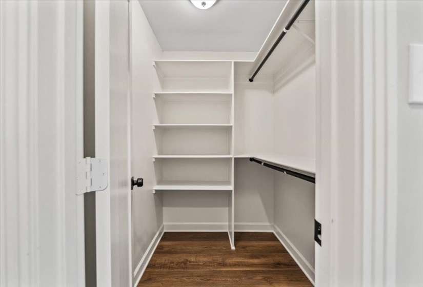 Walk-in closet featuring white built-in shelving, two hanging rods, and wood-finish flooring