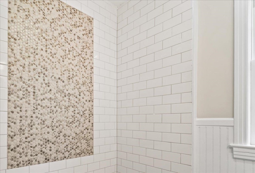 Shower enclosure featuring white subway tile walls and a decorative pebble-style tile accent panel