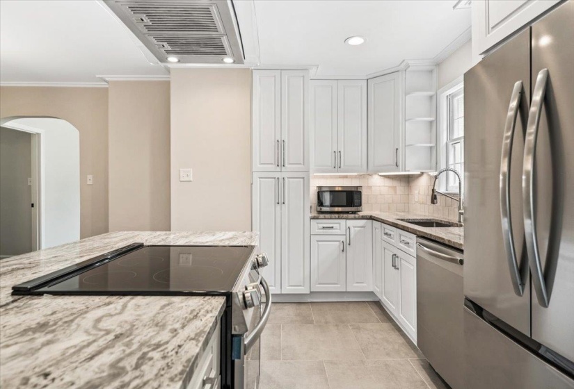 Modern kitchen featuring a large island with an electric cooktop, light-toned cabinetry, stainless steel appliances, and sleek countertops