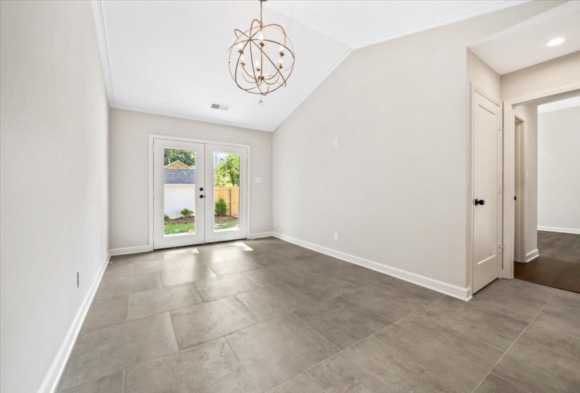Vaulted ceiling with an orb chandelier, double glass-paneled doors, neutral wall paint, tile flooring, and a solid interior door