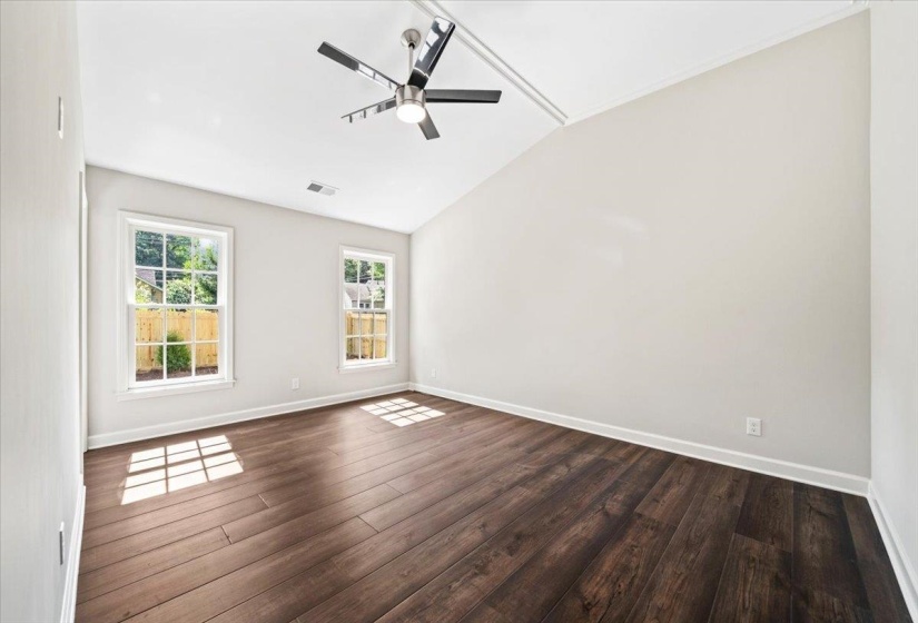 Spacious room featuring vaulted ceilings, two double-hung windows, wood-finish flooring, and a modern ceiling fan with lighting