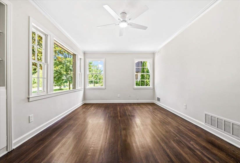 Spacious room with dark wood-finish flooring, white walls, and multiple windows