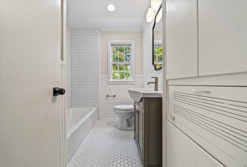 Full bathroom with white subway tile shower surround, hexagonal floor tiles, a window, beadboard wainscoting, and a vanity with an integrated sink