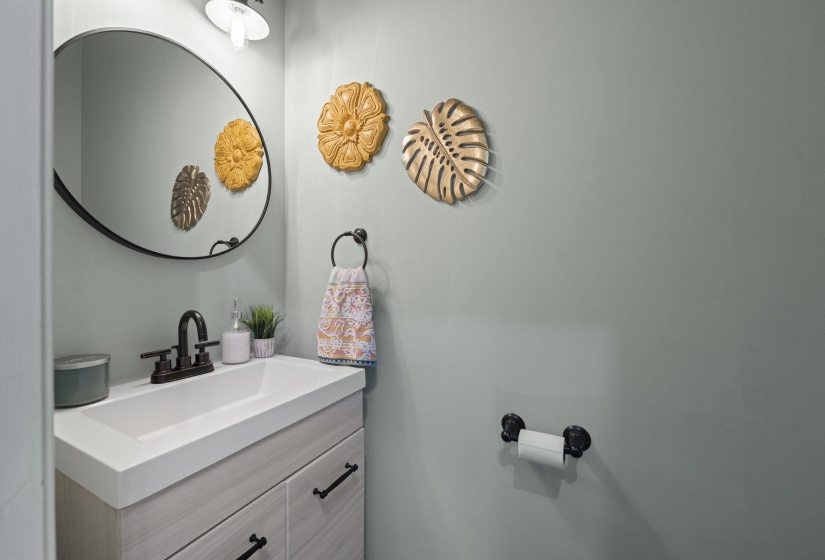 Vanity with integrated sink, black hardware, wood-finish cabinetry, and a round wall mirror