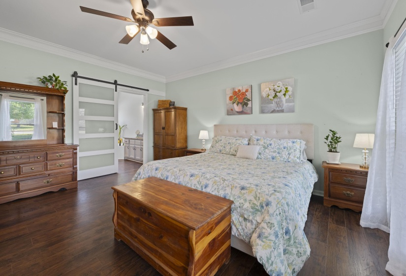 Spacious bedroom featuring wood-finish flooring, a contemporary ceiling fan, and a barn door with frosted glass panels
