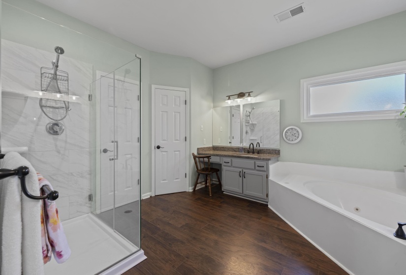 Bathroom featuring a glass-enclosed shower with tiled walls, a built-in jetted tub, and a dual-sink vanity with a stone-finish countertop