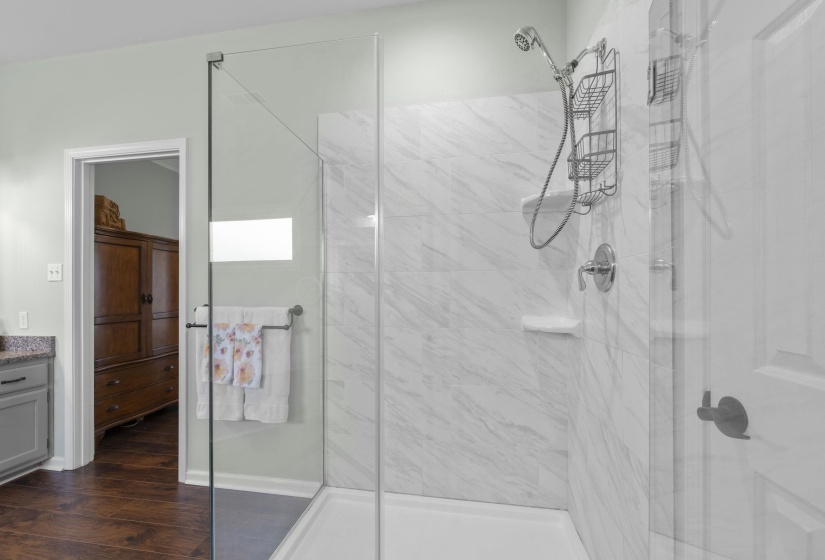 Glass-enclosed shower with white marble-look tile walls, chrome fixtures, and a handheld showerhead