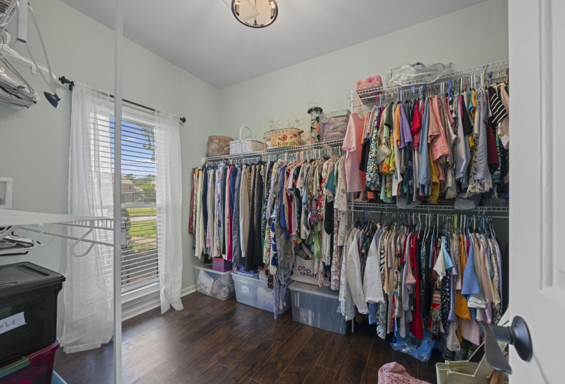 Spacious walk-in closet featuring wood-finish flooring, extensive built-in wire shelving, and a window with blinds