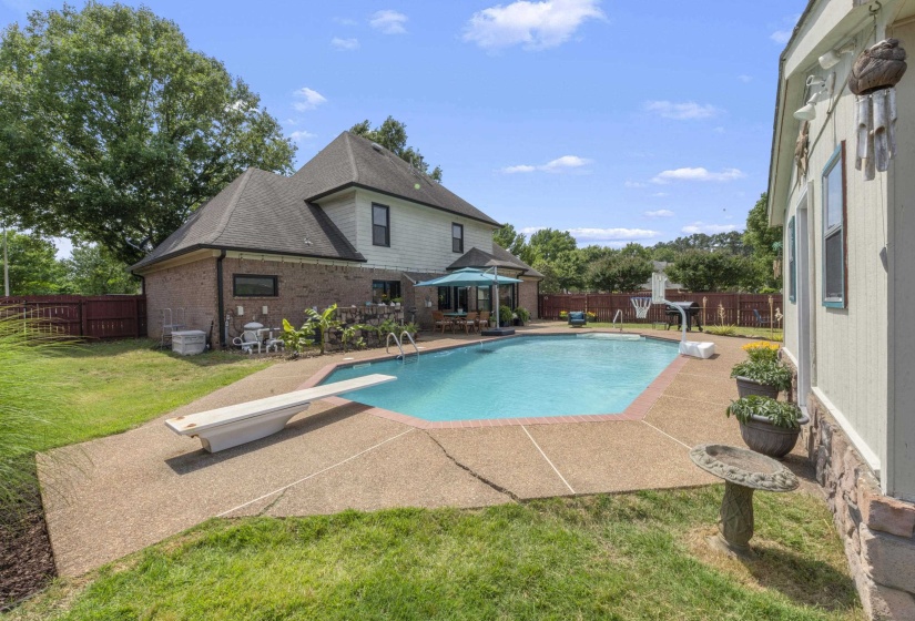 Expansive backyard featuring a large in-ground swimming pool, a diving board, and a surrounding aggregate concrete deck