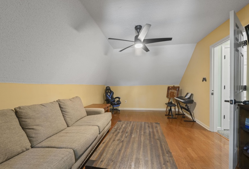 Spacious room featuring wood-finish flooring, a contemporary ceiling fan with integrated lighting, and a sloped ceiling with a textured finish
