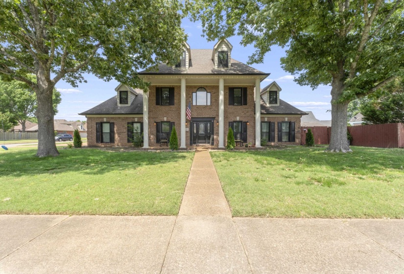 Two-story brick facade residence featuring a prominent columned portico, dormer windows, and a central arched window above the double entry doors