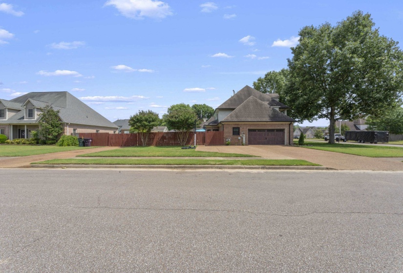 Brick exterior featuring a two-car garage with a wood-finish door, a dark shingle roof, and a mature tree providing shade