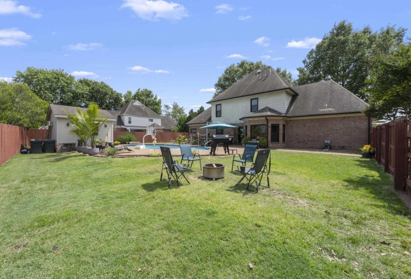 Expansive backyard featuring a large in-ground swimming pool, a dedicated pool house, a brick patio, and a privacy fence