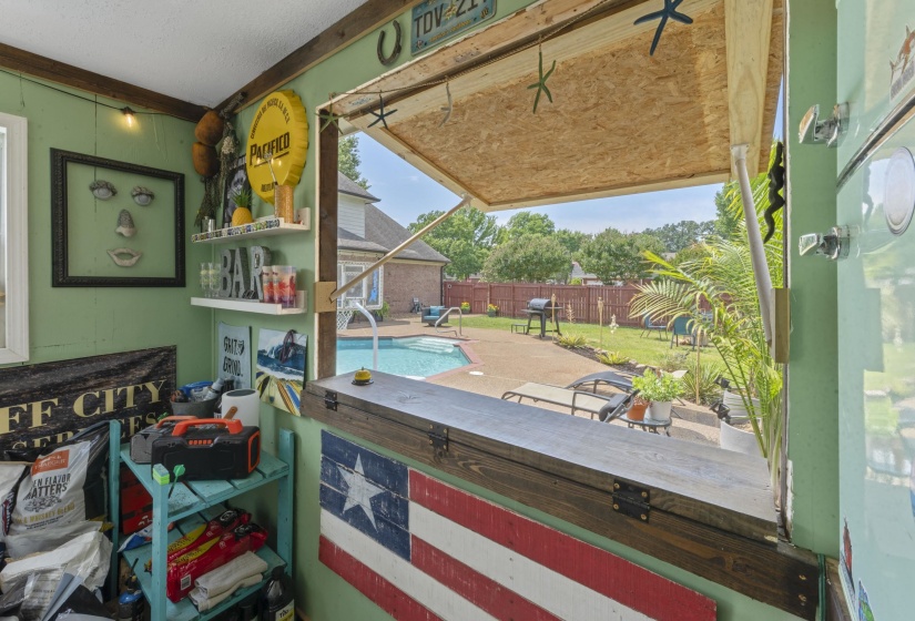 Outdoor entertainment space featuring a serving window with a wood-finish countertop, opening to a private backyard with an in-ground swimming pool, concrete patio, and a fenced perimeter