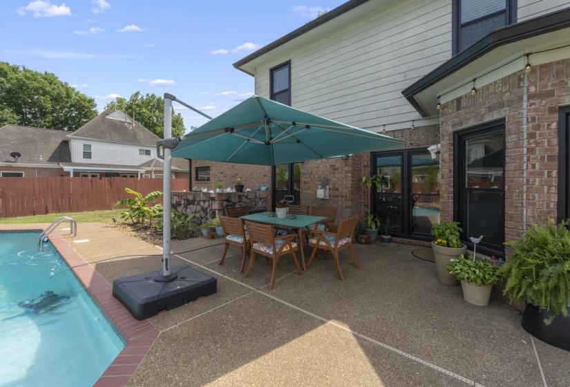 Brick and siding exterior featuring a concrete patio with an inground pool, dark-framed windows, and double patio doors