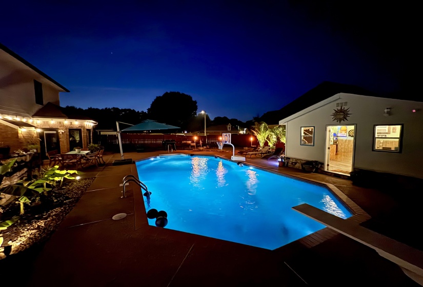 Illuminated swimming pool with diving board, surrounded by concrete decking