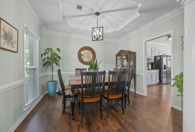 Formal dining area featuring wood-finish flooring, an ornate tray ceiling with crown molding, and a contemporary chandelier