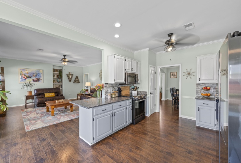 Open-concept kitchen featuring wood-finish flooring, white upper cabinetry, grey lower cabinetry, and dark countertops