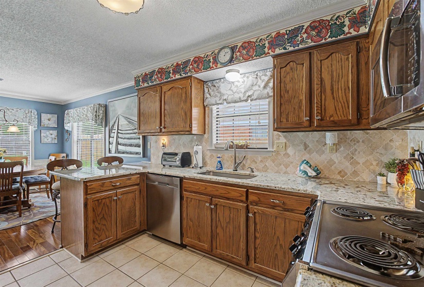 Kitchen featuring wood cabinetry, light-toned granite countertops, and a full tile backsplash