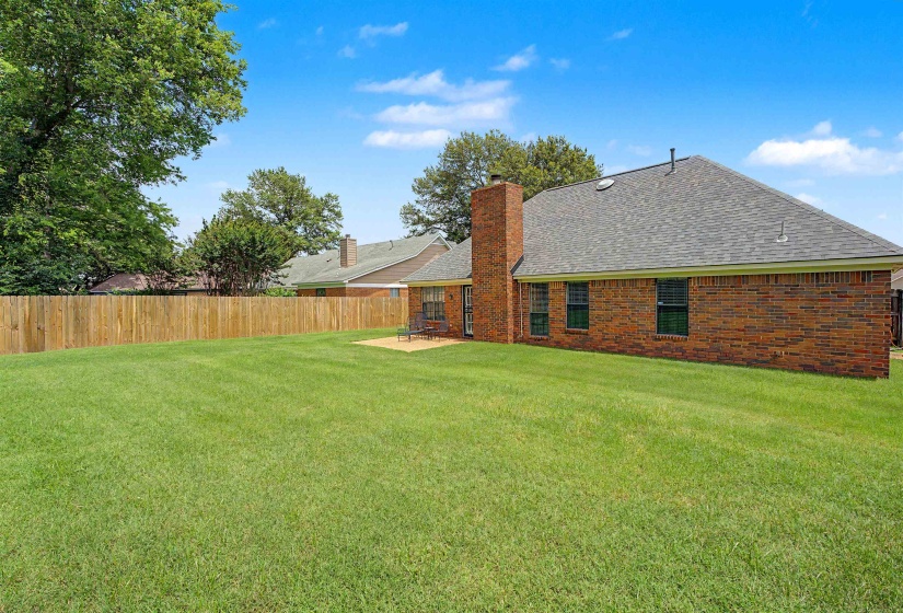 Expansive grass lawn featuring a wood privacy fence and a brick exterior with a pitched shingle roof