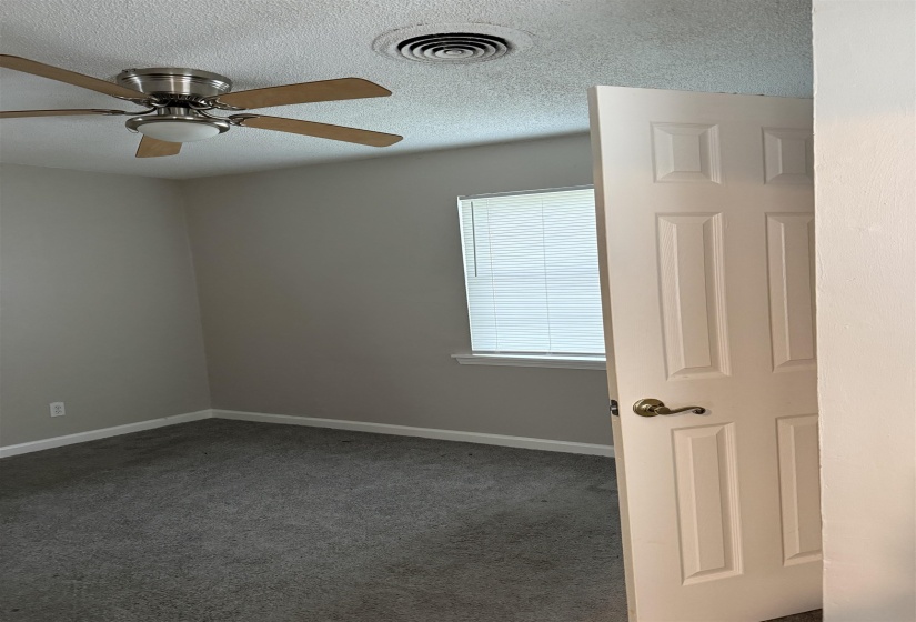Carpeted interior room featuring light gray walls, a window with horizontal blinds, a white paneled door with brass hardware, and a ceiling fan with light kit