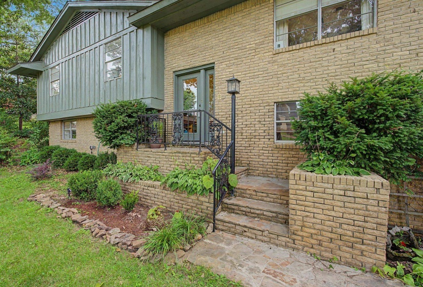 Exterior facade featuring a combination of brick and vertical panel siding, multiple windows, an outdoor lamp post, and a stone walkway leading to an entry door with wrought iron railing