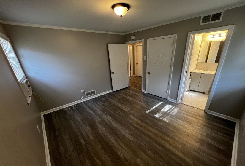 Unfurnished bedroom featuring dark wood-type flooring, crown molding, and ensuite bathroom