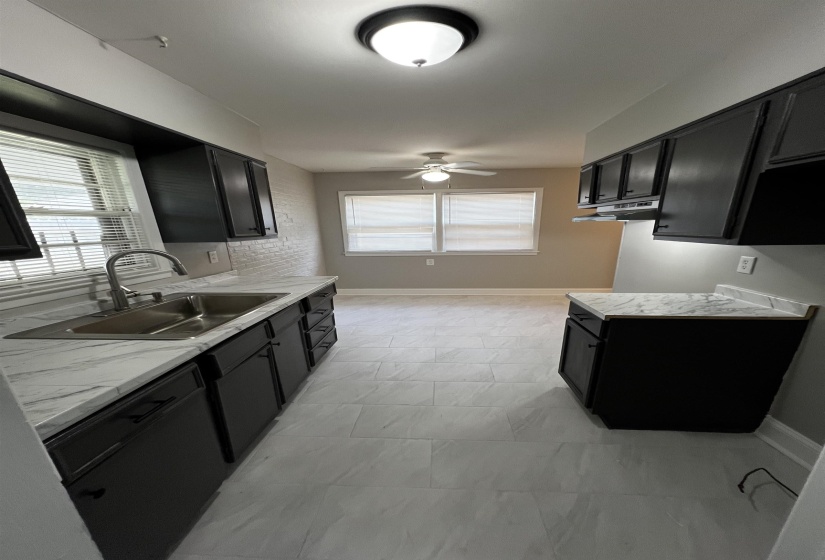 Kitchen featuring dark cabinets, light marble finish floors, ceiling fan, and under cabinet range hood