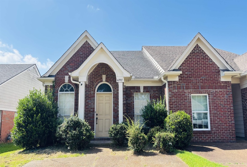 Brick facade residence featuring an arched entryway, gabled rooflines, and mature front landscaping