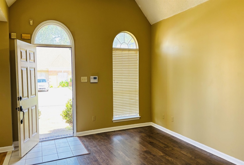 Entryway featuring an arched door with sidelight, vaulted ceiling, and wood-finish flooring