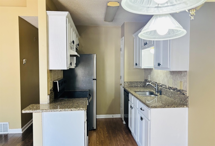 Kitchen featuring white cabinetry, granite-finish countertops, stainless steel refrigerator, and wood-finish flooring