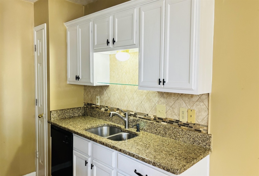 Kitchen featuring white shaker-style cabinetry, granite-finish countertops, stainless steel double basin sink, mosaic tile backsplash, and integrated dishwasher