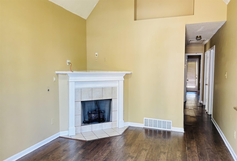 Living area featuring a fireplace with a white mantel and tiled surround, vaulted ceiling, wood-finish flooring, and a hallway entry
