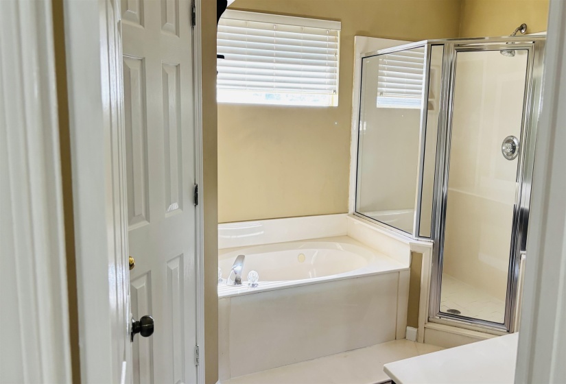 Bathroom with a built-in jetted tub, a glass-enclosed shower, and a window with horizontal blinds