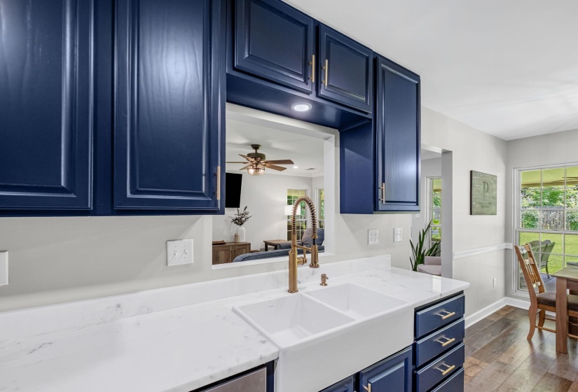 Kitchen featuring navy cabinetry with brass hardware, a white farmhouse-style double sink with a brass faucet, and white countertops