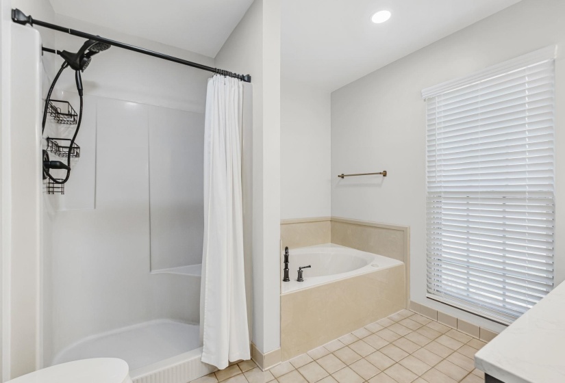 Bathroom featuring a built-in tub with dark-finish fixtures, a separate shower with a curved shower rod, and tile flooring