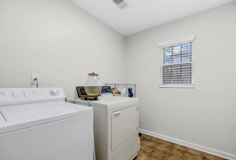 Dedicated laundry room featuring white walls, brown tile flooring, and a single window with blinds