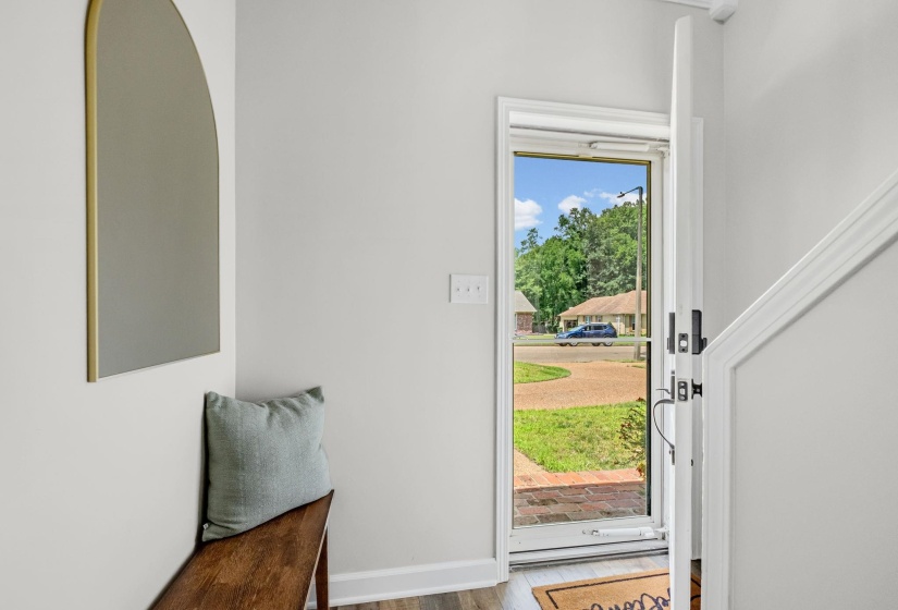 Bright entryway with light gray walls, wood-finish flooring, a white trim staircase, and a glass-paneled front door