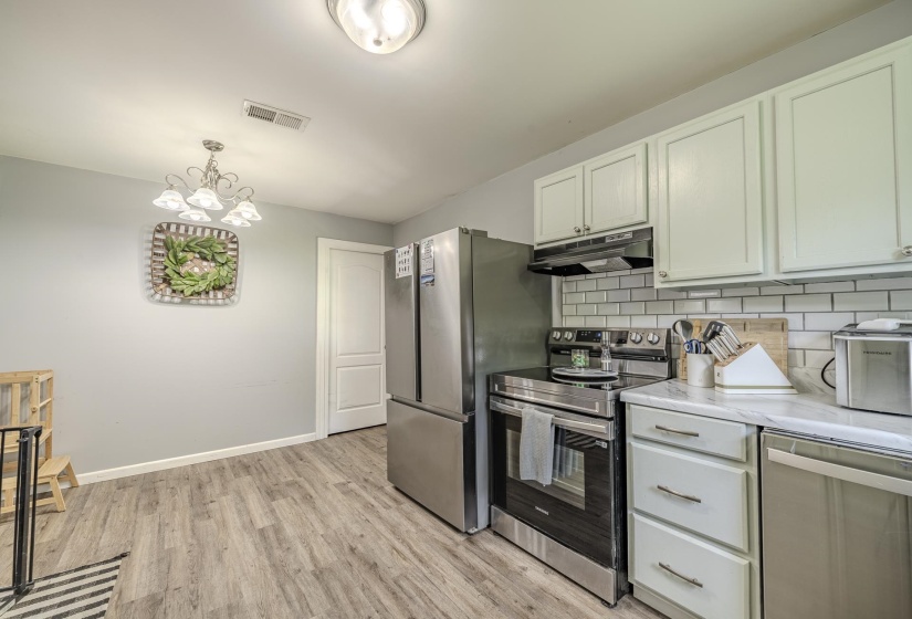 Kitchen featuring wood-finish flooring, light-toned cabinetry, stainless steel appliances, and a white subway tile backsplash