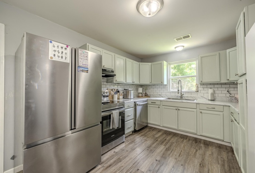 Kitchen featuring light-toned cabinetry, stainless steel appliances, a subway tile backsplash, and wood-finish flooring