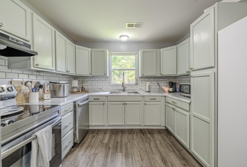 U-shaped kitchen featuring light-toned cabinetry, white subway tile backsplash, and wood-finish flooring