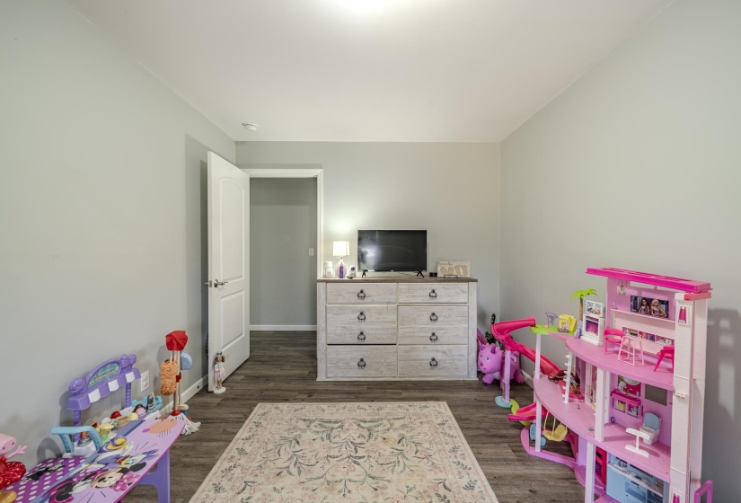 Spacious room featuring light gray walls, wood-finish flooring, and a white interior door