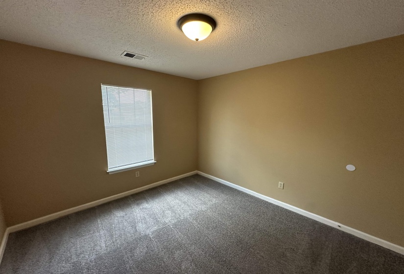 Room featuring neutral-toned walls, textured ceiling, a window with blinds, and dark gray carpeting